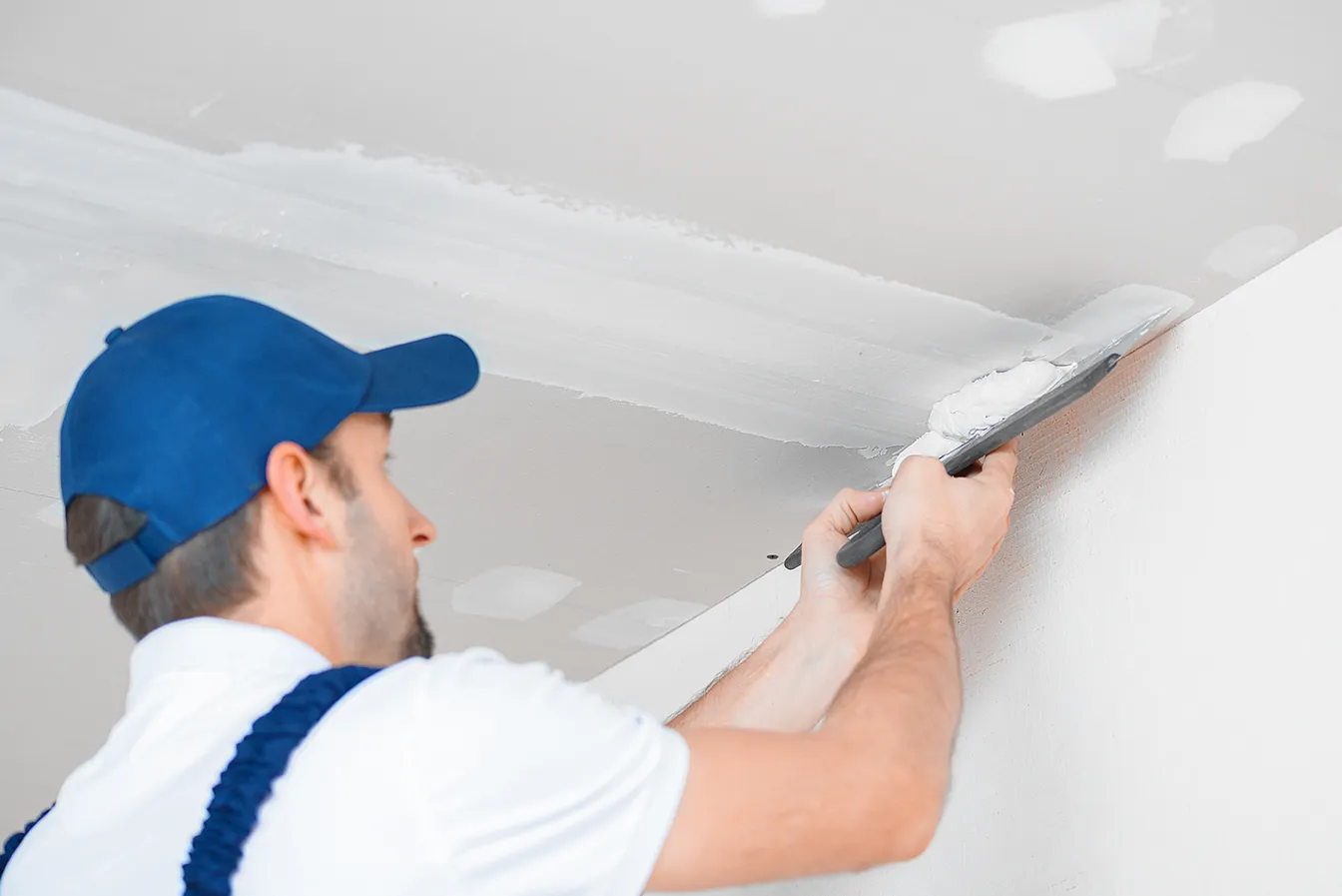 27stock-photo-a-master-in-uniform-applies-putty-with-a-spatula-to-the-reinforced-joint-of-drywall-on-the-ceiling-2055596843